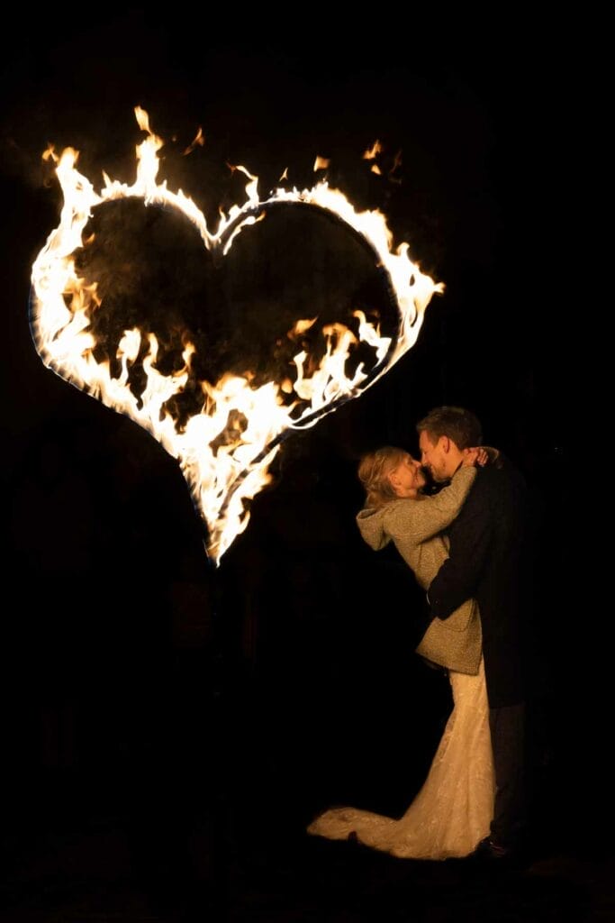 Ein Paar umarmt sich vor einem großen brennenden Herzen am Ende einer romantische und spektakulären Feuershow Hochzeit