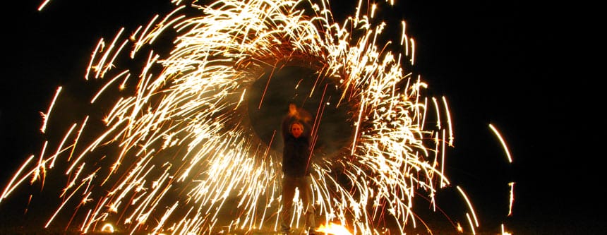 Der Feuerkünstler dreht einen Kreis aus hellen, funkelnden Pyroregen vor einem dunklen Hintergrund.